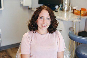 Young woman in pale pink tee shirt smiling in dental chair