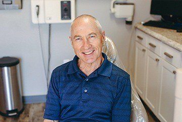 Man in dark blue polo shirt smiling in dental chair