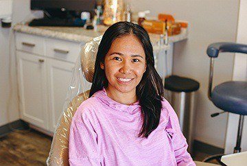 Young woman smiling in dental chair and wearing pink blouse
