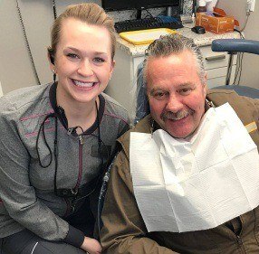 Dental team member and senior man in dental chair smiling together